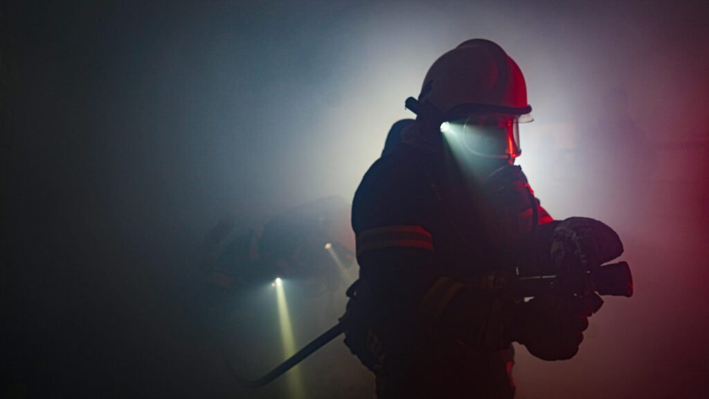 Firefighter in action with helmet and flashlight navigating through thick smoke, showcasing bravery and heroism.