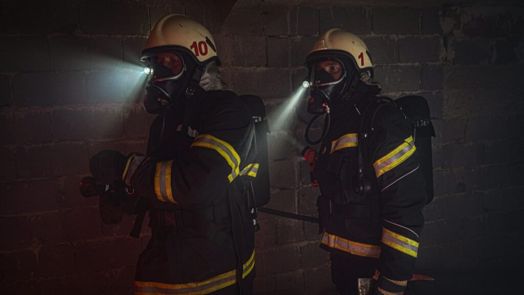 Firefighters in full gear working in dark conditions with flashlights.